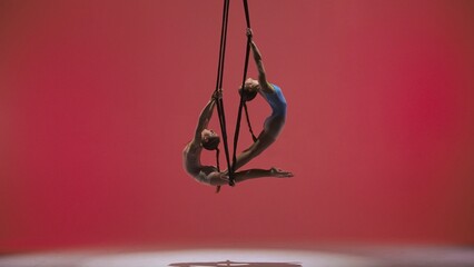 Female gymnastic duo isolated on red studio background. Girls aerial dancers spinning on acrobatic...