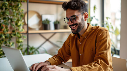 Man smiling while working on a laptop in a modern office environment