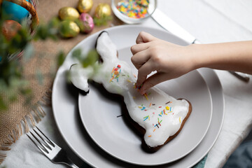 Hand of child decorating baked Easter bunny gingerbread cookie with multi colored sugar sprinkles....