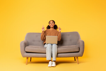 black student girl pointing fingers up sitting with laptop, studio