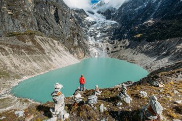 Female trekker dressed bright red jacket on the rock enjoying a glacier falling in high altitude...