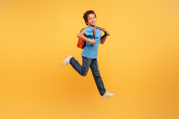 Fototapeta na wymiar Joyful boy jumping with backpack on vibrant yellow background