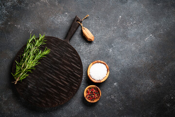 Food background at black kitchen table. Spices, herbs and craft cutting board. Flat lay with space for text.