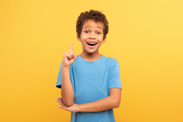 Excited boy with idea, finger raised up on yellow background