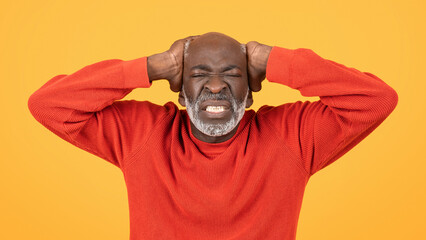 Frustrated senior man in a red sweater and hat, clutching his head with a grimace