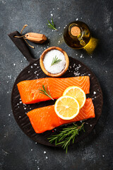Raw fish at black table. Salmon fillet with lemon and spices. Flat lay.