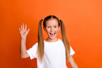 Photo portrait of pretty small girl waving excited hand hello wear trendy white outfit isolated on orange color background