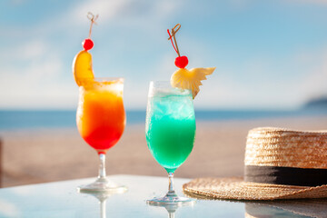 Tropical cocktails on sunny beach with straw hat. Summer vacation and travel.