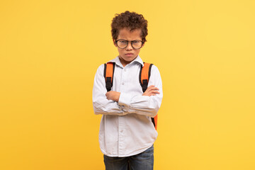 Angry latin schoolboy with arms crossed on yellow background