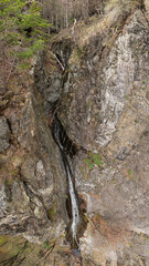 Aerial drone of a tall waterfall formed by a small spring falling from a vertical, abrupt cliff or stone wall. The gorges are located in Cozia National Park. Carpathia, Romania. Springtime season.