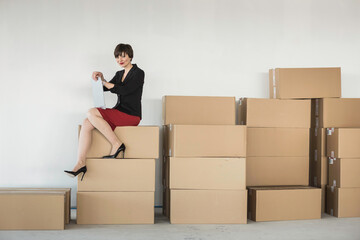 Female owner of a startup sits on top of moving boxes in the office with business plan in hand.