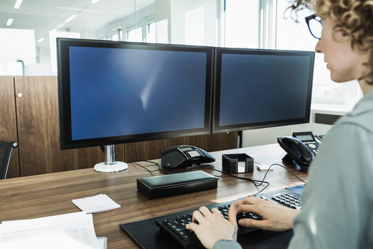 hands typing at desk two monitors