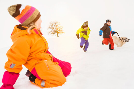 Three young kids running and playing in the snow in winter with their dog. Wolfratshausen, Bavaria, Germany 
