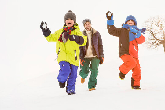 Two boys having a snowball fight and playing in the snow with their father in winter. Wolfratshausen, Bavaria, Germany 