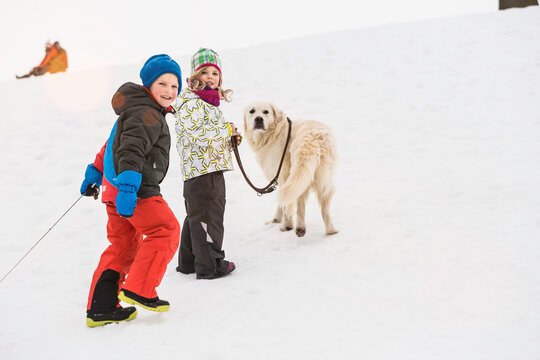 Young kids pulling their sled to the top of a hill in winter. Wolfratshausen, Bavaria, Germany 