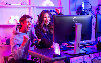 Couple or friends have shocking, exciting face with fun, using joystick to compete and play games together, sitting in room at home with neon decorated light. Game online streamer Concept.