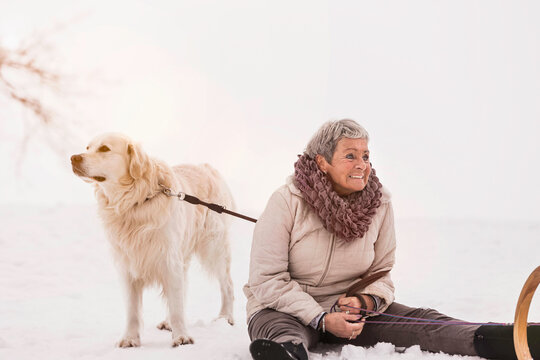 Older woman sitting in the snow in winter while holding her dog. Wolfratshausen, Bavaria, Germany