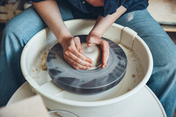 A young brunette potter at a potter's wheel. A middle-aged woman potter begins to shape a clay...