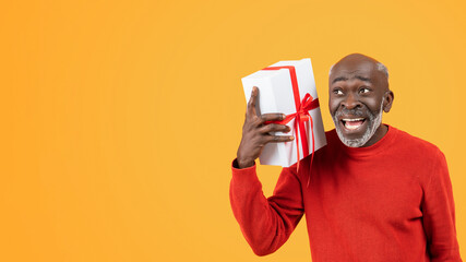 Joyful elderly African American man in a red sweater excitedly holding a white gift box