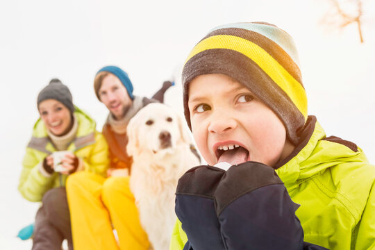 Mother, father and son drinking tea with their dog in a snowy landscape in winter. Wolfratshausen, Germany
