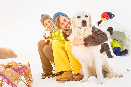 Mother, father and son petting their dog in a snowy landscape in winter. Wolfratshausen, Germany