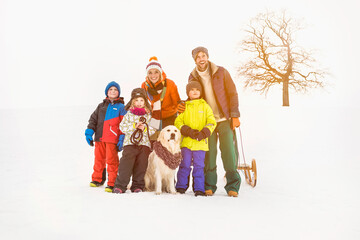 Young parents with 3 kids and a dog in snowy landscape before going sledding. Wolfratshausen, Germany