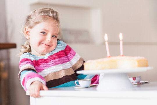 Young girl looking into the camera before blowing out the candles on her birthday cake. Munich, Germany