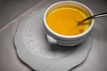 Traditional and homemade bowl of pumpkin soup with spoon on white plate.