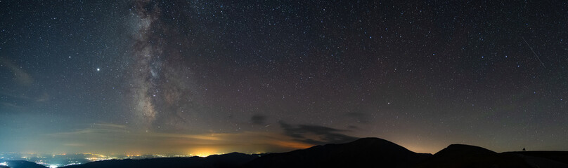 Milky way seen seen from the mountains, rising above urban city pollution in a summer night. Horizon is lit in orange. Sky is full with stars and constellations. Milky way's core is up.