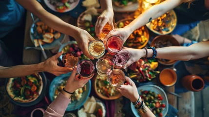 Fotobehang Top view of a group of people sitting around a rustic wooden dining table, toasting with their glasses raised amidst a spread of various dishes © MP Studio