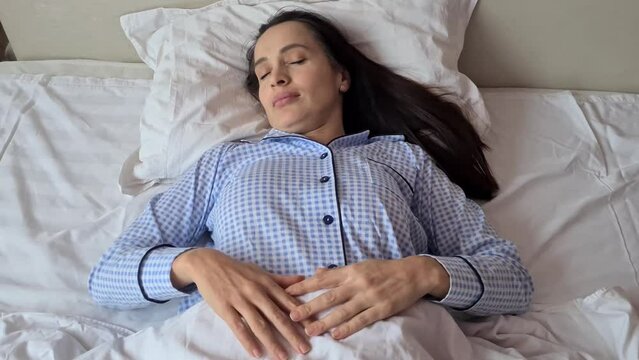 Shocked young beautiful woman overslept and quickly gets up lying in bed. Beautiful girl wakes up holds head in hands and screams and realizes overslept in morning