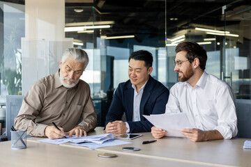 Three businessmen collaborating on financial documents in a bright office environment, depicting teamwork, strategy, and professionalism. - obrazy, fototapety, plakaty
