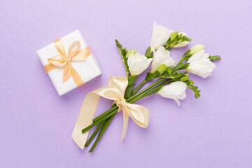 Gift box with freesia flower on color background, top view