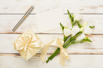 Gift box with freesia flower with card on wooden background, top view