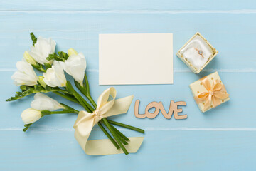 White freesia flower and gift box with diamond ring on wooden background, top view