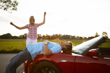 Couple dancing and laughing in front of their new red convertible sports car. Munich, Bavaria, Germany