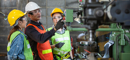 Asian foreman manager showing case study of factory machine to two engineer trainee young woman in...