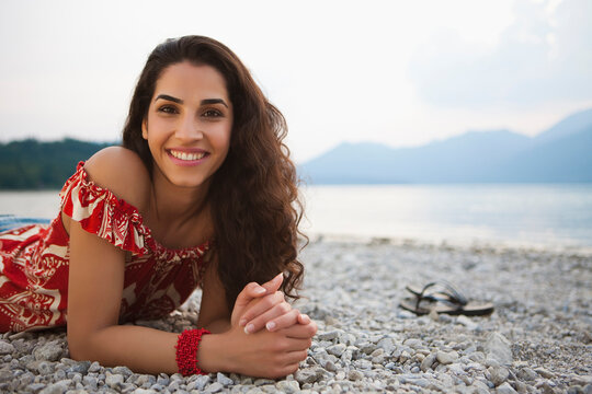 Woman smiling in the camera while lying on the gravel beach of a lake. Walchensee, Germany