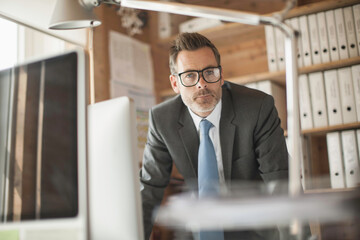 Confident young business man at a start-up business looking into the camera with colleagues in the background.
