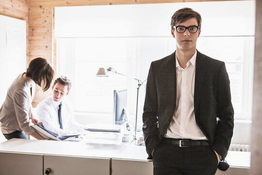 Confident young business man at a start-up business looking into the camera with colleagues in the background.