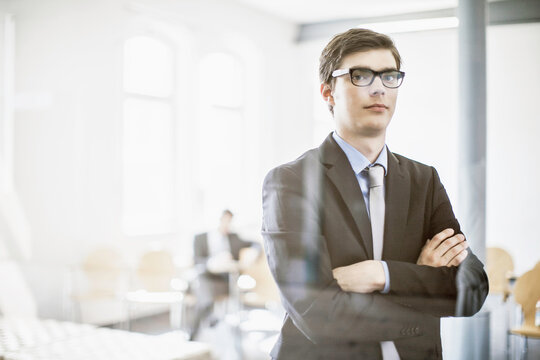 Confident young business man at a start-up business looking into the camera with colleagues in the background.