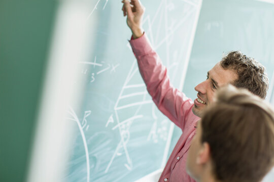 Dozent mit Sch&uuml;lerin an Tafel lim Klassenzimmer