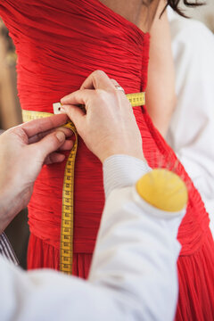 Beautiful dark skinned woman is being fitted in an evening gown by fashion designer and his 3 tailors. Munich, Bavaria, Germany