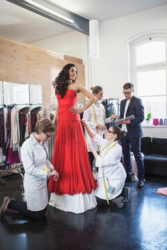 Beautiful dark skinned woman is being fitted in an evening gown by fashion designer and his 3 tailors. Munich, Bavaria, Germany