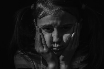Cute little sad offended child girl is crying on a black background. Black and white image.