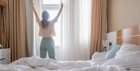 Woman stretching standing by window after wake up, back view