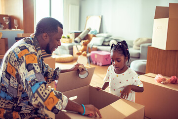 Father sealing moving box with daughter at home