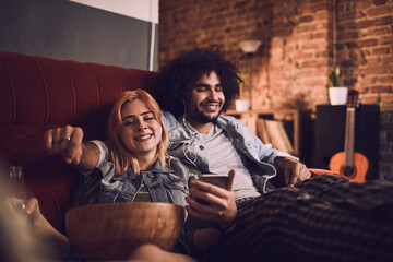 Relaxed couple sharing music on a couch with snacks and drinks