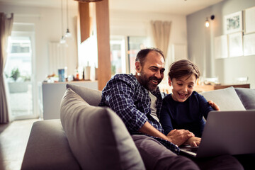 Happy father and son having fun with laptop on the couch