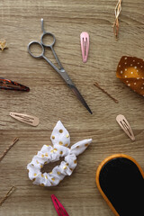 Wooden hairbrush, scissors and various headbands, hair clips and scrunchies on wooden background. Flat lay.